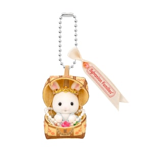 May include: A Sylvanian Families keychain featuring a white rabbit wearing a gold crown and pearl necklace, inside a yellow patterned chest. The chest is attached to a silver chain and a ribbon with the brand name.