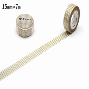 Puede incluir: Un rollo de cinta washi con patrón de cuadrícula en beige y blanco y una tira de la misma cinta extendida. La cinta está etiquetada como 15mm x 7m y presenta el logotipo de la marca mt deco en el núcleo. El diseño consiste en una cuadrícula.