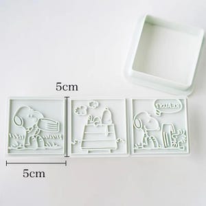 three square cookie cutouts of characters from the Peanuts comic strip, including Snoopy, Woodstock, and Charlie Brown.