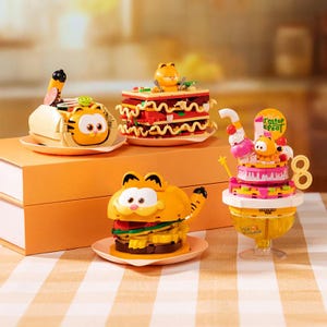 Könnte beinhalten: Eine Sammlung von orangefarbenen und gelben Garfield-Spielzeugbausteinen. Die Spielzeuge zeigen ein Sandwich, eine Lasagne, einen Kuchen und ein Auto. Jedes Spielzeug zeigt Garfield's Gesicht und andere Details.