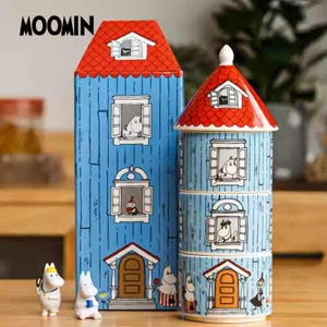 May include: A blue and red Moomin house-shaped container and a stackable container with a red roof. The containers feature illustrations of Moomin characters in windows and at the doors. The word "MOOMIN" is printed at the top.