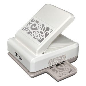 May include: A white and gray paper punch with a decorative floral design. The punch has a rectangular shape with a hinged top and a tray to catch the punched-out paper. The word "DECOP" is printed on the side.