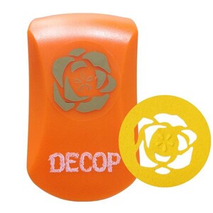 May include: An orange craft punch featuring a rose design and the word "DECOP" in pink. A yellow, circular paper cutout of the rose is next to the punch. The punch has a rounded top and a flat bottom.