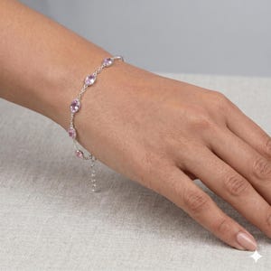 May include: A silver chain bracelet featuring a series of evenly spaced, oval-shaped light pink gemstones set in polished metal bezels. The delicate link chain includes a small extender section with a lobster claw clasp at the end of the bracelet.