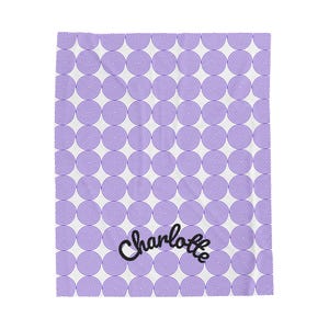 Könnte beinhalten: Eine weiße rechteckige Decke mit einem sich wiederholenden Muster aus violetten Spiralkreisen. Der Name Charlotte ist in einer schwarzen Schreibschrift im unteren mittleren Bereich des Stoffes aufgedruckt.