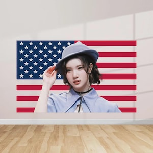 May include: A person wearing a blue hat and a blue collared shirt, posing in front of a large American flag. The flag features red and white stripes and a blue field with white stars. The person is wearing a black choker.