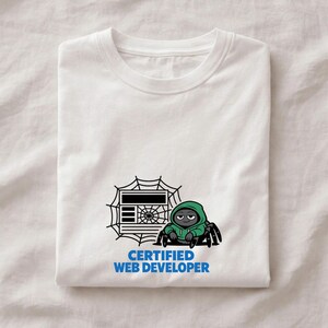 May include: White t-shirt with a cartoon spider in a green hoodie, a web design, and a computer screen graphic. The blue text reads "CERTIFIED WEB DEVELOPER". The t-shirt is folded neatly. A fun design for web developers.