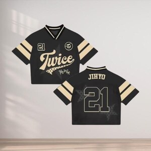 May include: Black and beige cropped jersey with the word "Twice" in a stylized font, the number "21", and a star graphic. The jersey has beige stripes on the sleeves and collar. The back of the jersey displays the name "JIHYO" and the number "21".