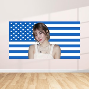 Puede incluir: Una gran obra de arte mural que presenta a una persona frente a un diseño de bandera estadounidense azul y blanco. La persona lleva una camiseta blanca y tiene el pelo corto castaño. El fondo es una pared de color claro y un suelo de madera.