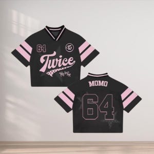 May include: Black crop top jersey with pink accents and the number 64. The front features the word "Twice" in a script font, and the back displays "MOMO" and the number 64. The jersey has a v-neck collar and striped sleeves.