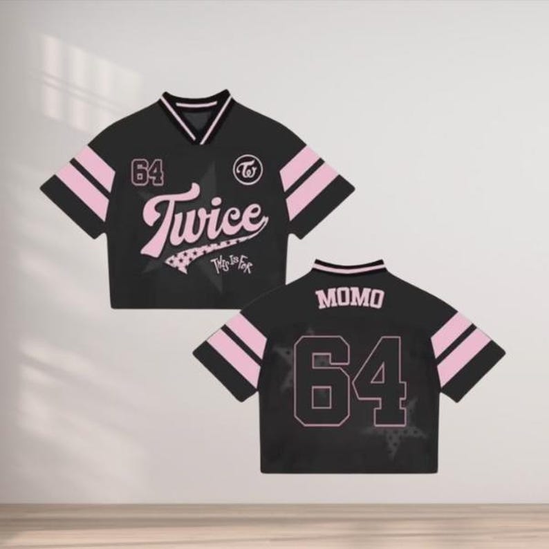 May include: Black crop top jersey with pink accents and the number 64. The front features the word "Twice" in a script font, and the back displays "MOMO" and the number 64. The jersey has a v-neck collar and striped sleeves.