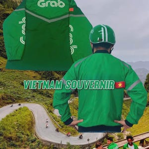 Puede incluir: Chaqueta verde con la palabra "Grab" en la espalda y la capucha. La chaqueta tiene rayas reflectantes y el texto "VIETNAM SOUVENIR" en la espalda. Una bandera vietnamita está en el hombro derecho. La chaqueta es un recuerdo.