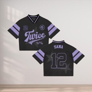 May include: Black cropped jersey with purple accents. Features the word "Twice" in a stylized font, the number "12", and the name "Sana" on the back. Includes a star design and a logo.