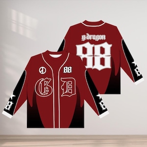 Puede incluir: Camiseta de béisbol burdeos con detalles blancos y mangas negras. La parte trasera muestra el número "98" y el texto "g-dragon". La parte delantera presenta las letras "G" y "D", el número "88" y un símbolo de la paz.