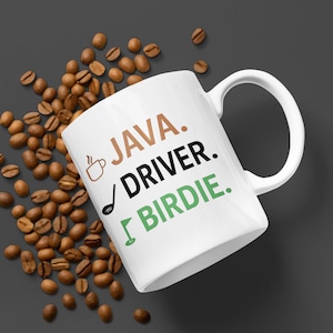 May include: White ceramic mug with the words "JAVA. DRIVER. BIRDIE." in brown, black, and green. A coffee cup and golf club icon are also featured. Coffee beans surround the mug on a dark gray surface.