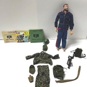 以下が含まれることがあります： 青い制服に赤い縁取りのG.I.ジョーのアクションフィギュア。迷彩柄のジャケットとパンツ、小さなヘルメット2つ、水筒、バックパック、ライフル、ストラップ、そしてArmy ManualとMarine Manualと書かれた3冊のミニチュア説明書が付属しています。