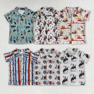 May include: Six short-sleeved button-down shirts with Western-themed patterns. Designs include cacti, cowboys, horses, and geometric shapes. Colors include turquoise, white, red, and brown. The shirts are likely for children.