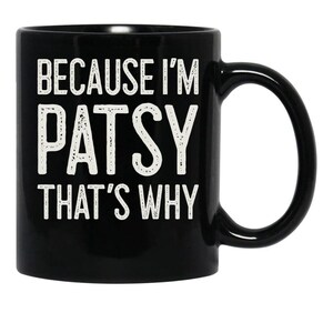 May include: Black ceramic mug with a curved handle. The mug features the white text "BECAUSE I'M PATSY THAT'S WHY" in a bold, sans-serif font. The mug is designed for hot beverages.