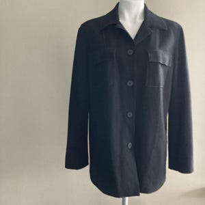 May include: A dark charcoal-colored jacket with a collared neckline and two chest pockets. The jacket has a button-down closure and long sleeves. The garment is displayed on a white mannequin.