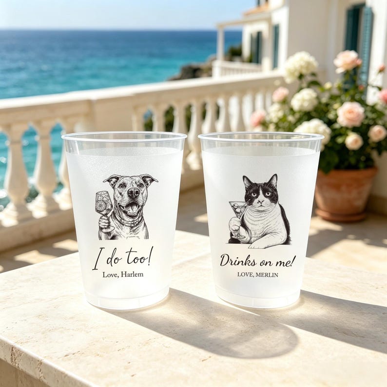 May include: Two frosted plastic cups featuring black and white illustrations of a dog and a cat holding cocktail glasses. The dog cup has the text 'I do too! Love, Harlem' and the cat cup has the text 'Drinks on me! LOVE, MERLIN' printed in black.