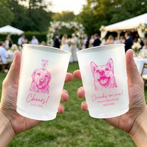 May include: Two frosted plastic cups featuring bright pink ink illustrations of dogs. The left cup shows a dog with a martini glass graphic and the text "Cheers! Love, Bella". The right cup shows a dog with the text "Drinks on me! Cheers to Mom & Dad! 09.23.2026".