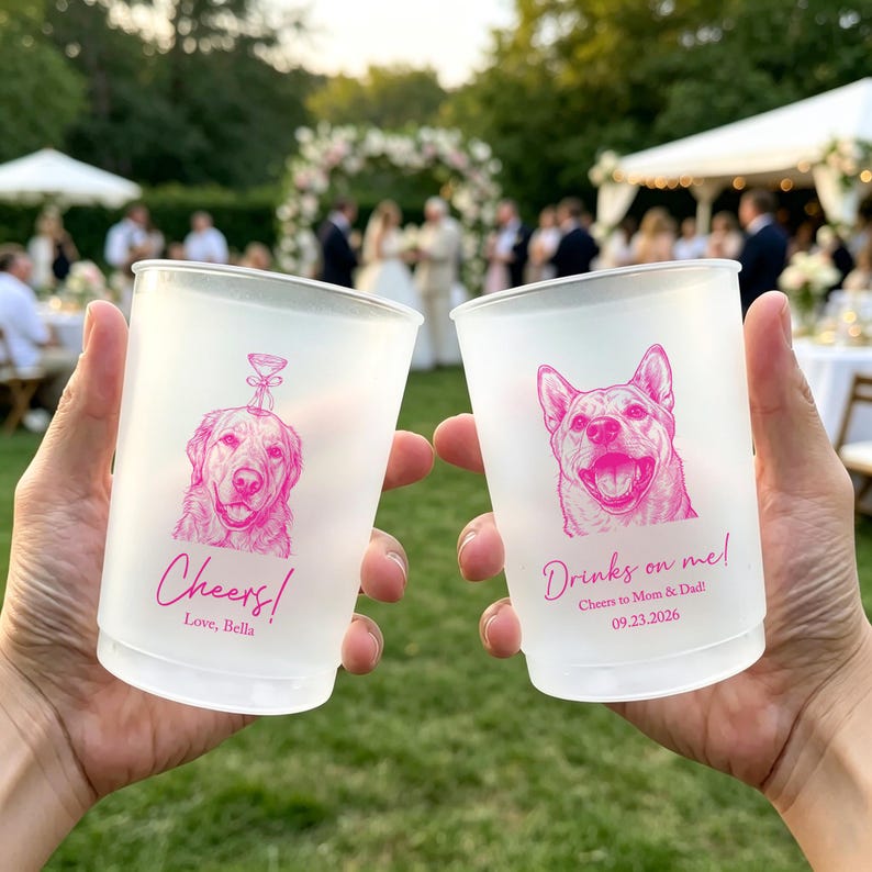 May include: Two frosted plastic cups featuring bright pink ink illustrations of dogs. The left cup shows a dog with a martini glass graphic and the text "Cheers! Love, Bella". The right cup shows a dog with the text "Drinks on me! Cheers to Mom & Dad! 09.23.2026".