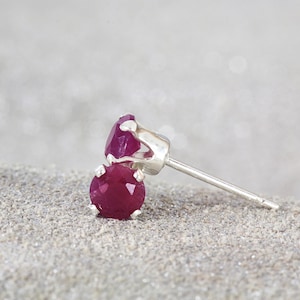 May include: A pair of ruby earrings with silver settings. The earrings are round and have a classic design.