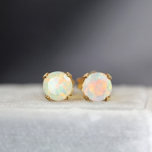 May include: A pair of gold stud earrings with white opal gemstones. The earrings are set in a simple, classic style.