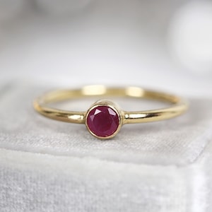 May include: A simple gold band ring with a single round ruby gemstone.