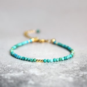 May include: A delicate turquoise and gold beaded bracelet with a sliding clasp. The bracelet features small, round turquoise beads and three gold beads in the centre.