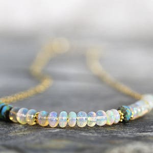 May include: A delicate gold chain necklace with a row of iridescent white opal beads and two blue and black gemstone accents.