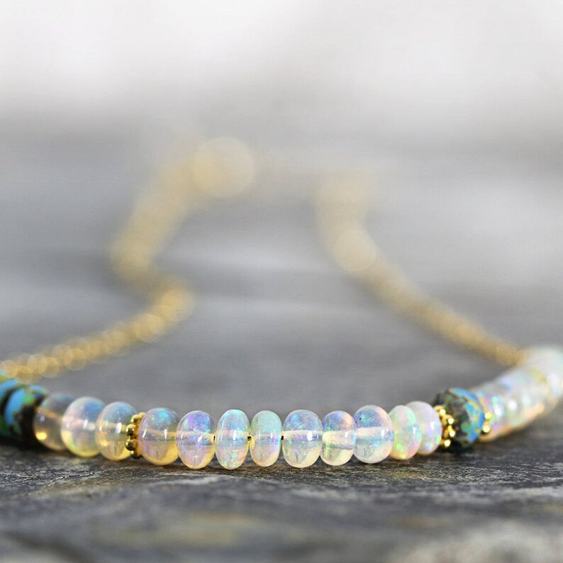 May include: A delicate gold chain necklace with a row of iridescent white opal beads and two blue and black gemstone accents.
