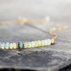 May include: A delicate gold chain necklace with a single row of small white opal beads and a blue accent bead.