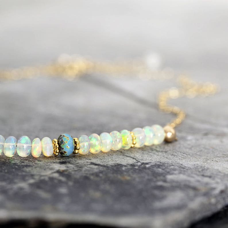 May include: A delicate gold chain necklace with a single row of small white opal beads and a blue accent bead.