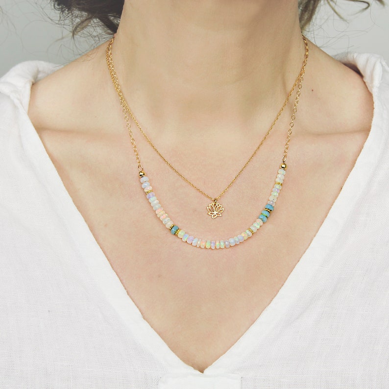 May include: A gold chain necklace with a delicate lotus flower pendant and a second chain with a row of pastel opal beads.