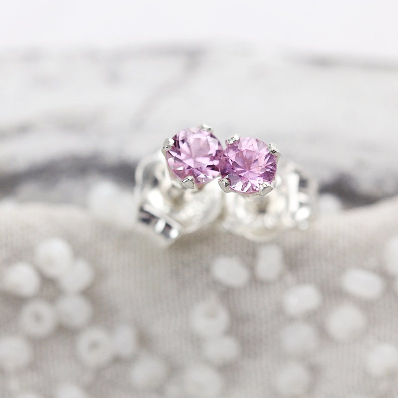 May include: A pair of silver stud earrings with small, round, light pink gemstones.