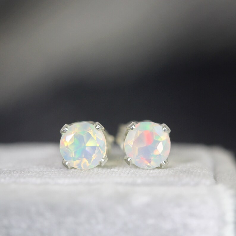 Puede incluir: Un par de pendientes de bot&oacute;n de &oacute;palo redondo. Los &oacute;palos tienen un color base blanco con destellos iridiscentes verdes, azules y rosas. Los pendientes est&aacute;n engastados en metal plateado con cuatro garras.