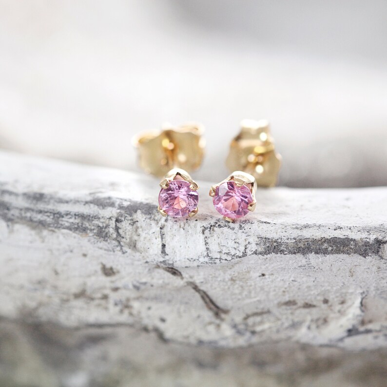 May include: A pair of gold stud earrings with small pink gemstones.