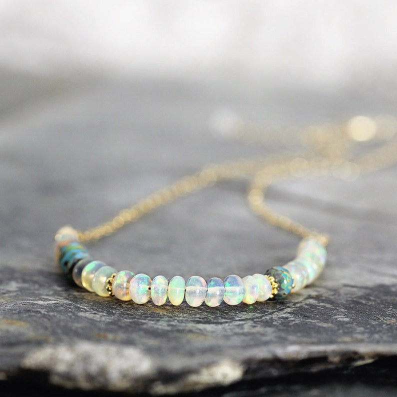 May include: A delicate gold chain necklace with a row of white opal beads. The necklace has a simple design and is perfect for everyday wear.