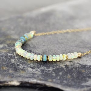 May include: A delicate gold chain necklace with a row of white opal beads and a single turquoise bead in the center.