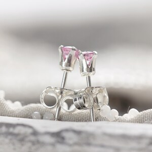 May include: A pair of silver stud earrings with pink gemstones. The earrings have a simple, classic design and are perfect for everyday wear.
