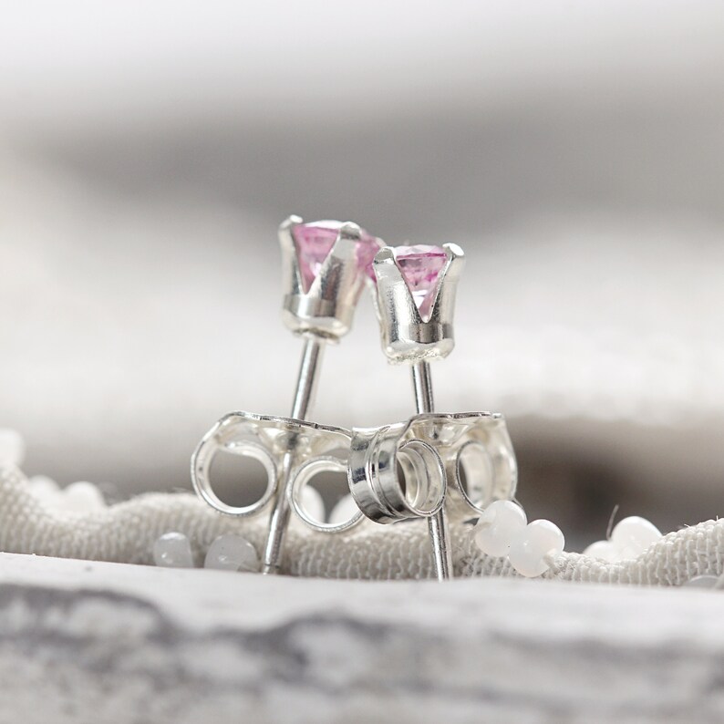 May include: A pair of silver stud earrings with pink gemstones. The earrings have a simple, classic design and are perfect for everyday wear.