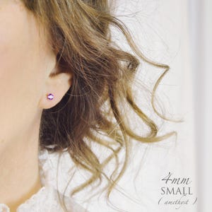 May include: A small 4mm round amethyst stud earring featuring a vibrant purple gemstone set in a simple metal prong setting. The earring is positioned on an earlobe, and the text 4mm SMALL (amethyst) is clearly visible in the bottom right corner.