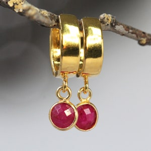 May include: Gold hoop earrings with dangling ruby red gemstone drops.