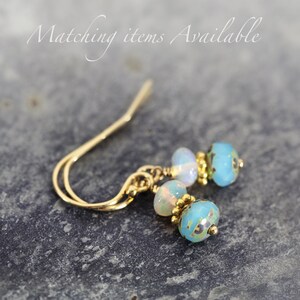 May include: Gold earrings with blue and white opal beads. The earrings have a simple, elegant design.
