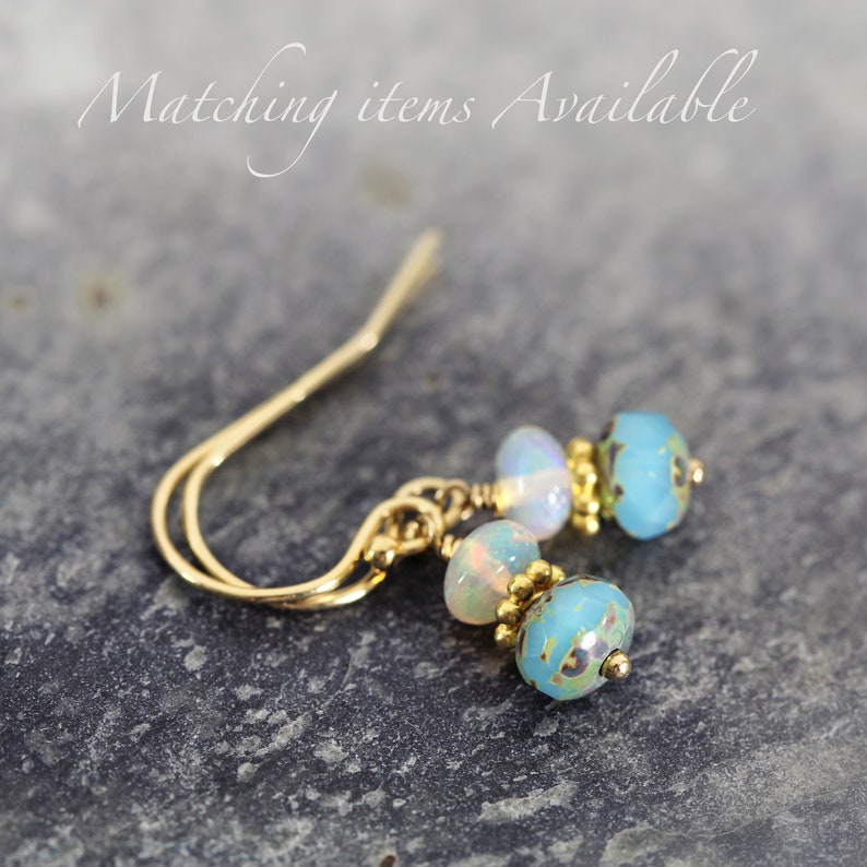 May include: Gold earrings with blue and white opal beads. The earrings have a simple, elegant design.