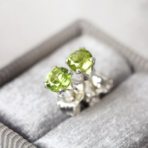 A pair of bright green gemstone stud earrings. The peridot gemstones are sparkling and catch the light. The stones are a brilliant round cut with lots of facets, and set into sterling silver four prong settings. Simple, minimal, round stud earrings.