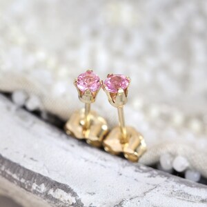 May include: A pair of gold stud earrings with pink gemstones. The earrings have a simple design and are perfect for everyday wear.
