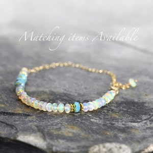 May include: A delicate gold chain bracelet with a row of white opal beads and a single turquoise bead in the center.