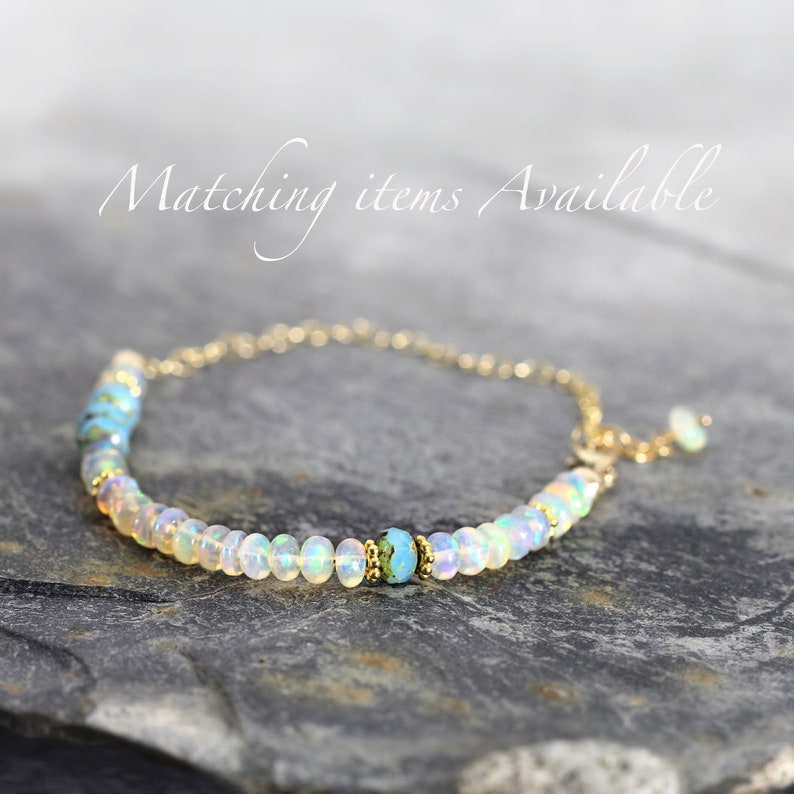 May include: A delicate gold chain bracelet with a row of white opal beads and a single turquoise bead in the center.